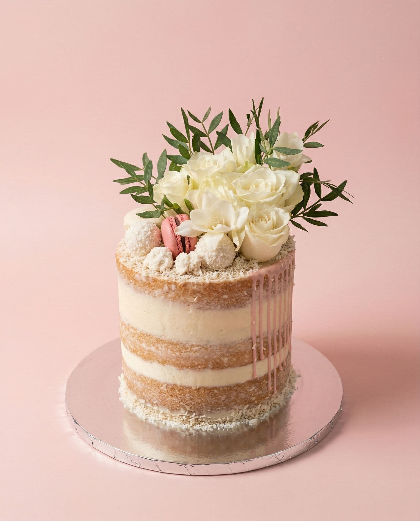 The same cake photographed on a blush backdrop with even light, so the pink drip and the layers read clearly