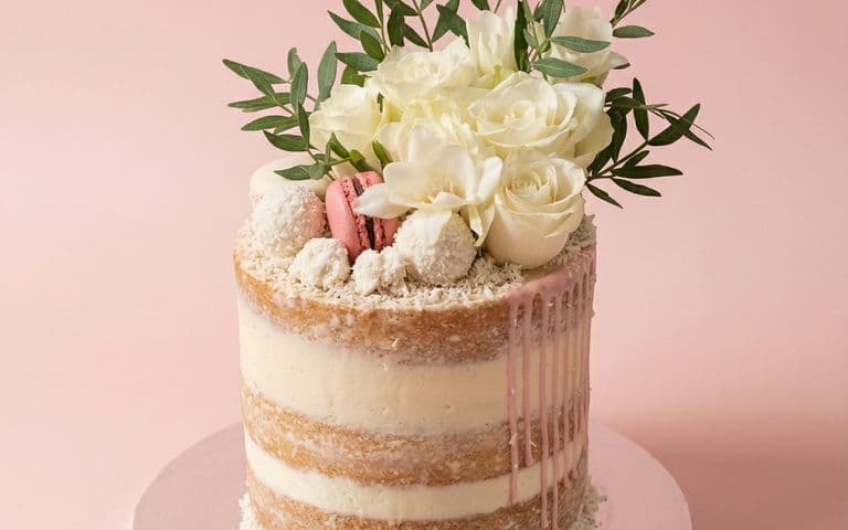 The same cake photographed on a blush backdrop with even light, so the pink drip and the layers read clearly