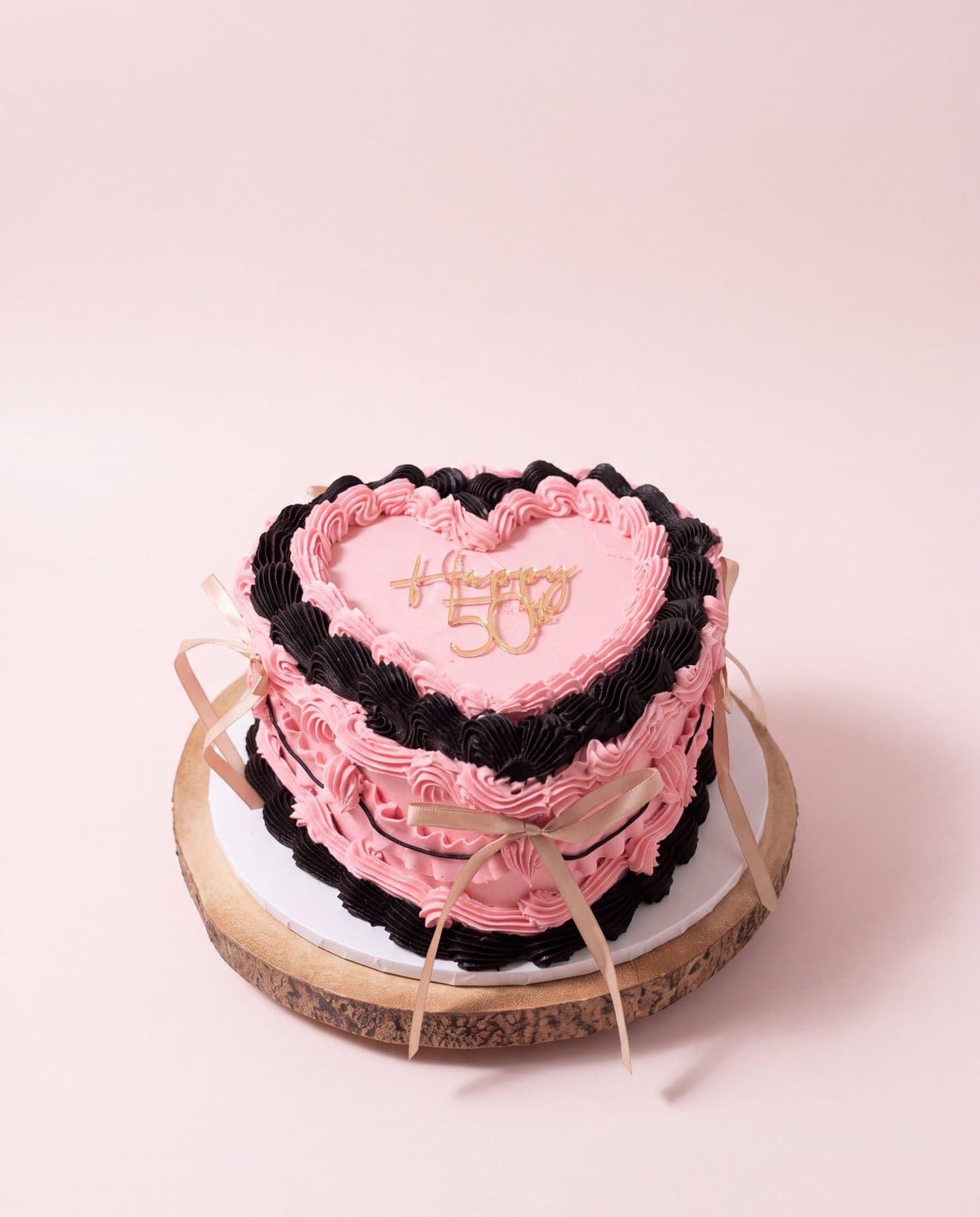 Pink heart cake with black piping and a gold Happy 50th topper